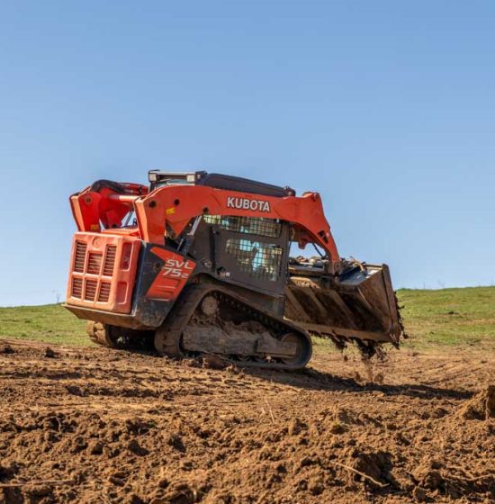 A bulldozer is being used to level a field; it is moving dirt across a grassy field.