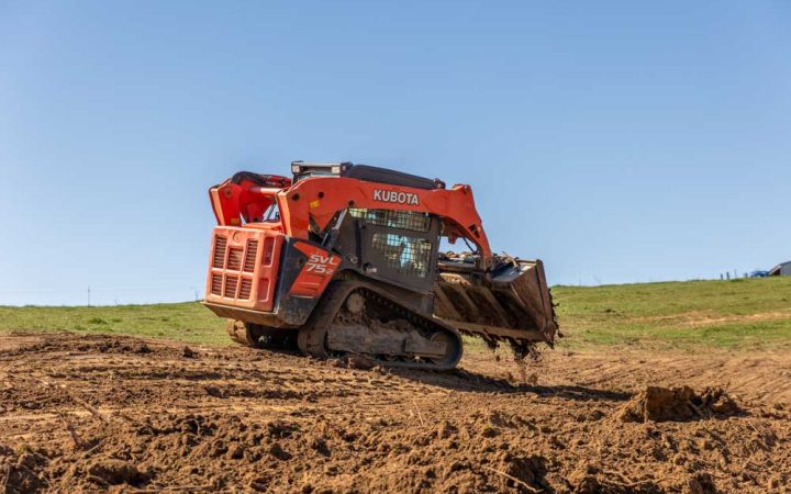 A bulldozer is being used to level a field; it is moving dirt across a grassy field.