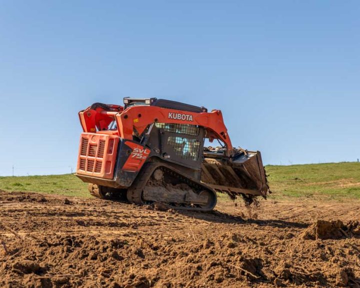 A bulldozer is being used to level a field; it is moving dirt across a grassy field.