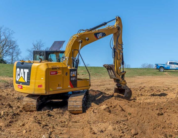 A yellow excavator with a large bucket arm and treads, scooping up dirt at a construction site.