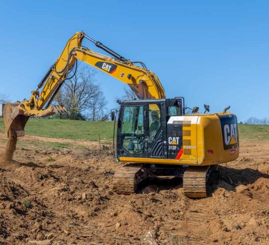 A powerful Caterpillar excavator with a massive hydraulic arm and treads, engaged in excavation work on a construction site. The excavator is actively digging into a dirt embankment, contributing to the land development process.