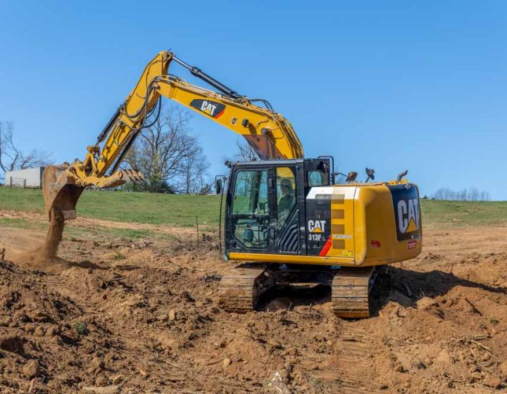 A powerful Caterpillar excavator with a massive hydraulic arm and treads, engaged in excavation work on a construction site. The excavator is actively digging into a dirt embankment, contributing to the land development process.