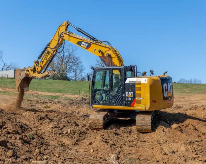A powerful Caterpillar excavator with a massive hydraulic arm and treads, engaged in excavation work on a construction site. The excavator is actively digging into a dirt embankment, contributing to the land development process.