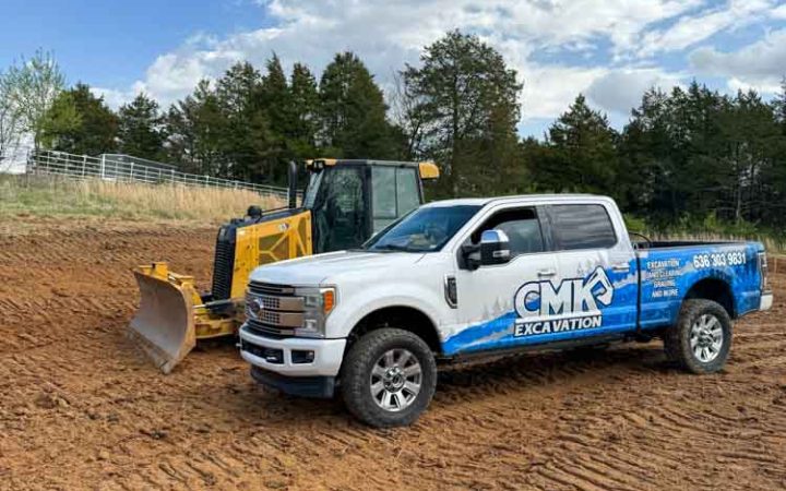 A construction site with a white pick-up truck of CMK Excavation and a yellow mini bulldozer.