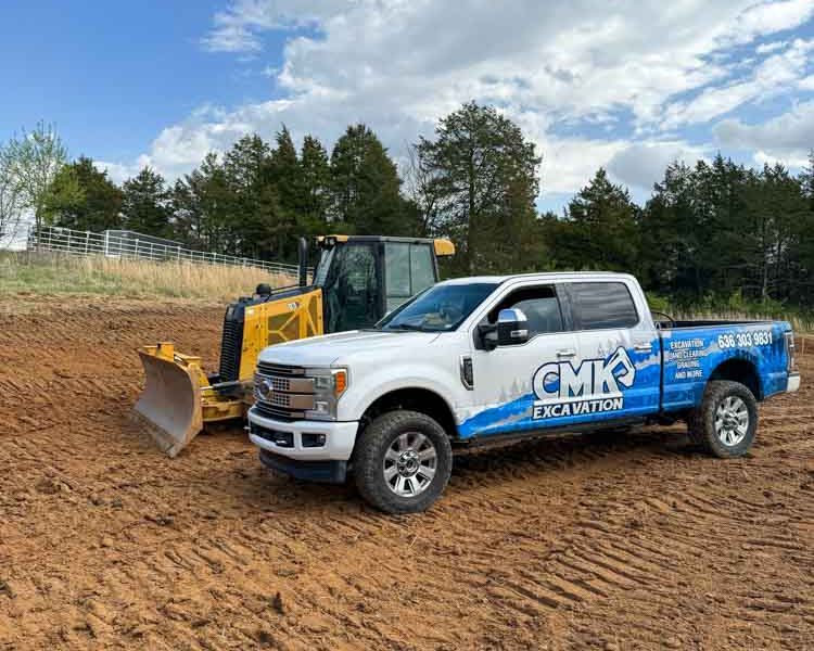 A construction site with a white pick-up truck of CMK Excavation and a yellow mini bulldozer.